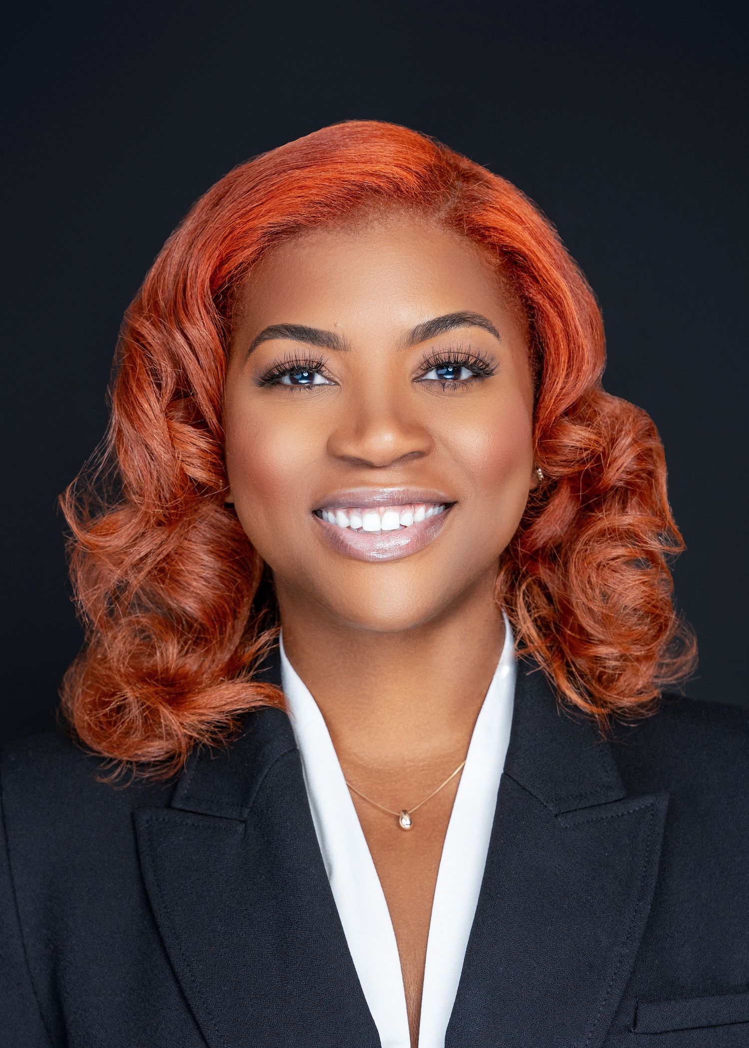 Studio portrait with copper-toned curled hair wearing professional black and white attire.