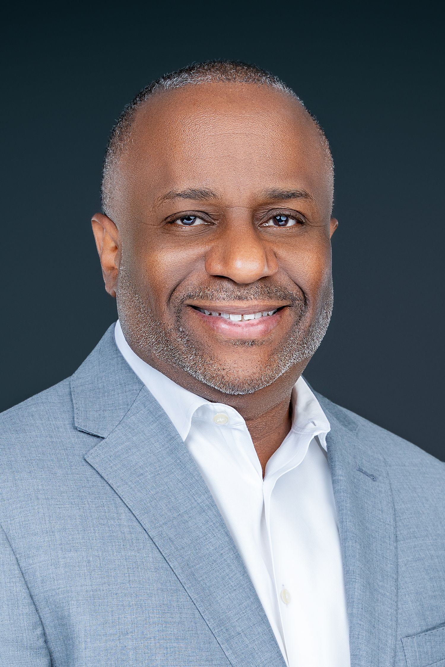 Executive portrait of person in light gray suit and white shirt against dark background.