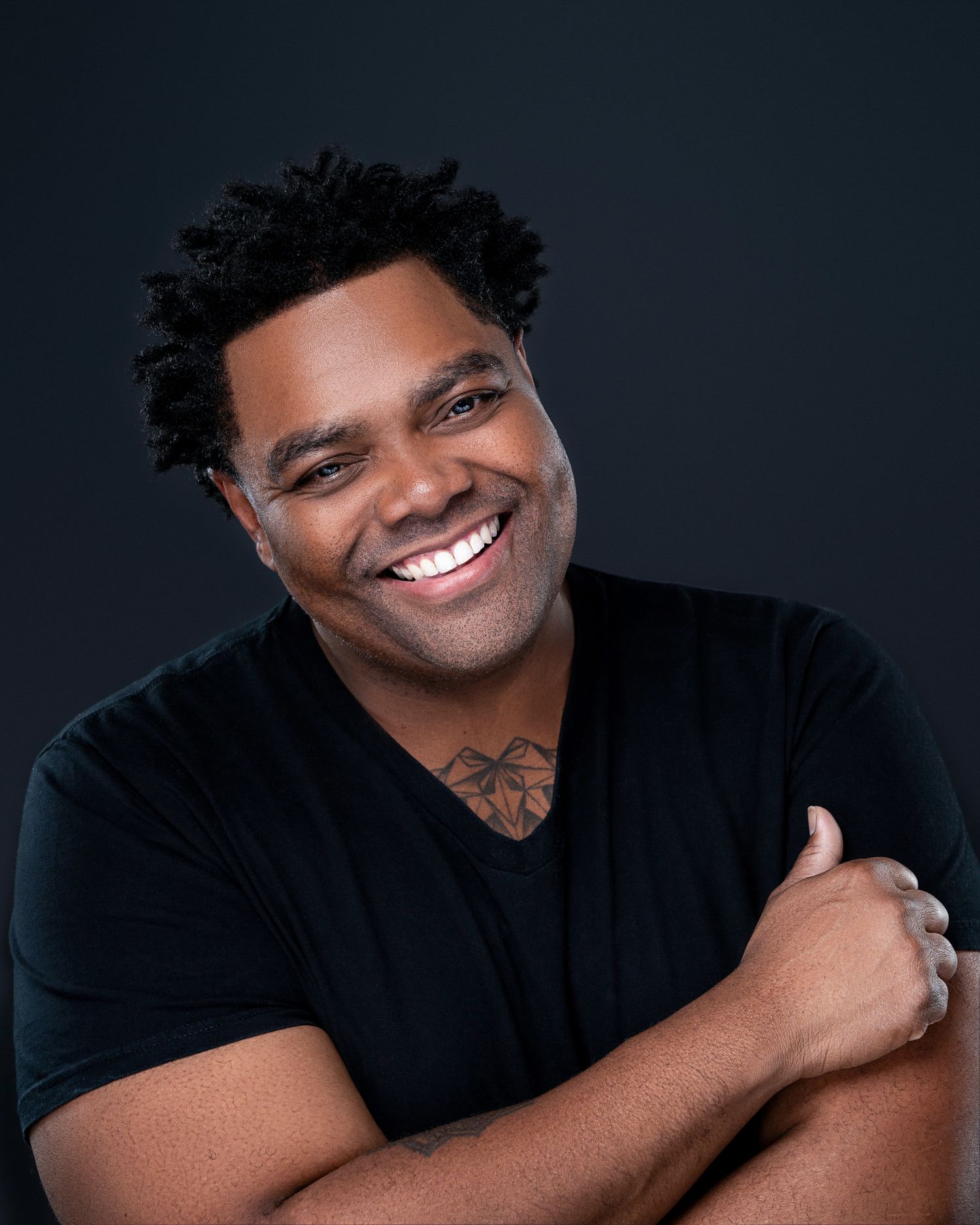 Casual portrait series of person in black t-shirt with bright smile against dark background.