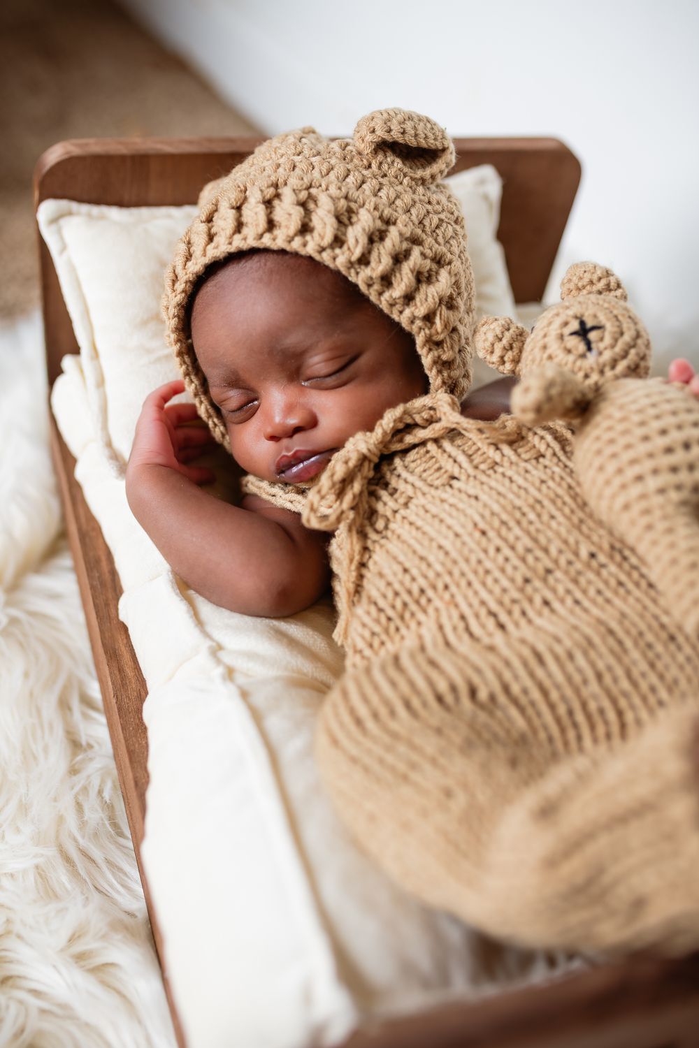 Sleeping newborn wearing knitted beige outfit rests peacefully on white bedding in a series of gentle poses.