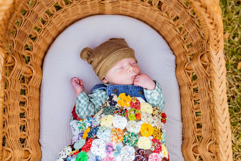 A sleeping baby lying in a wicker basket surrounded by colorful flowers and soft blankets.