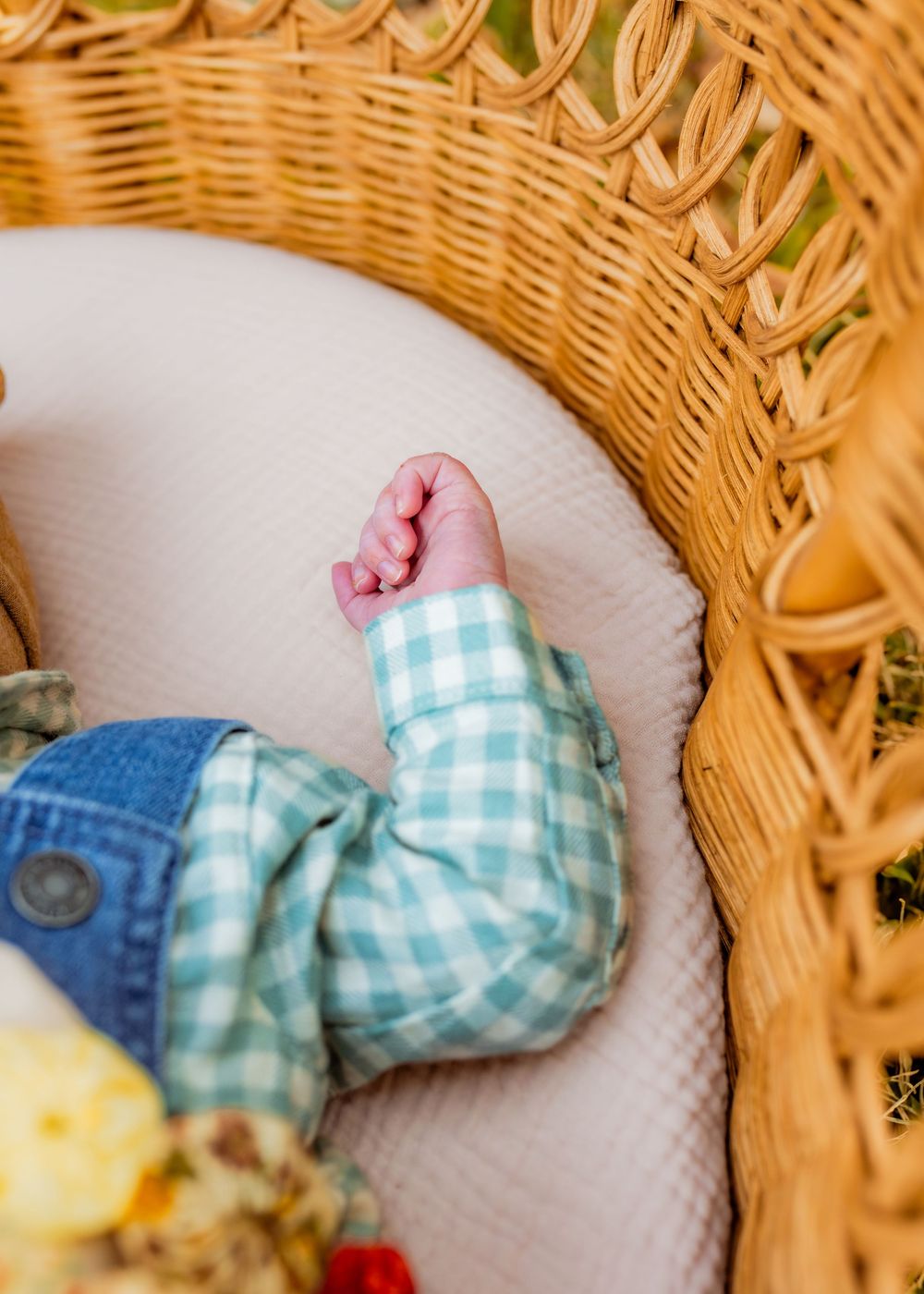 Tiny baby foot in mint gingham clothing rests on white cushion inside wicker basket.