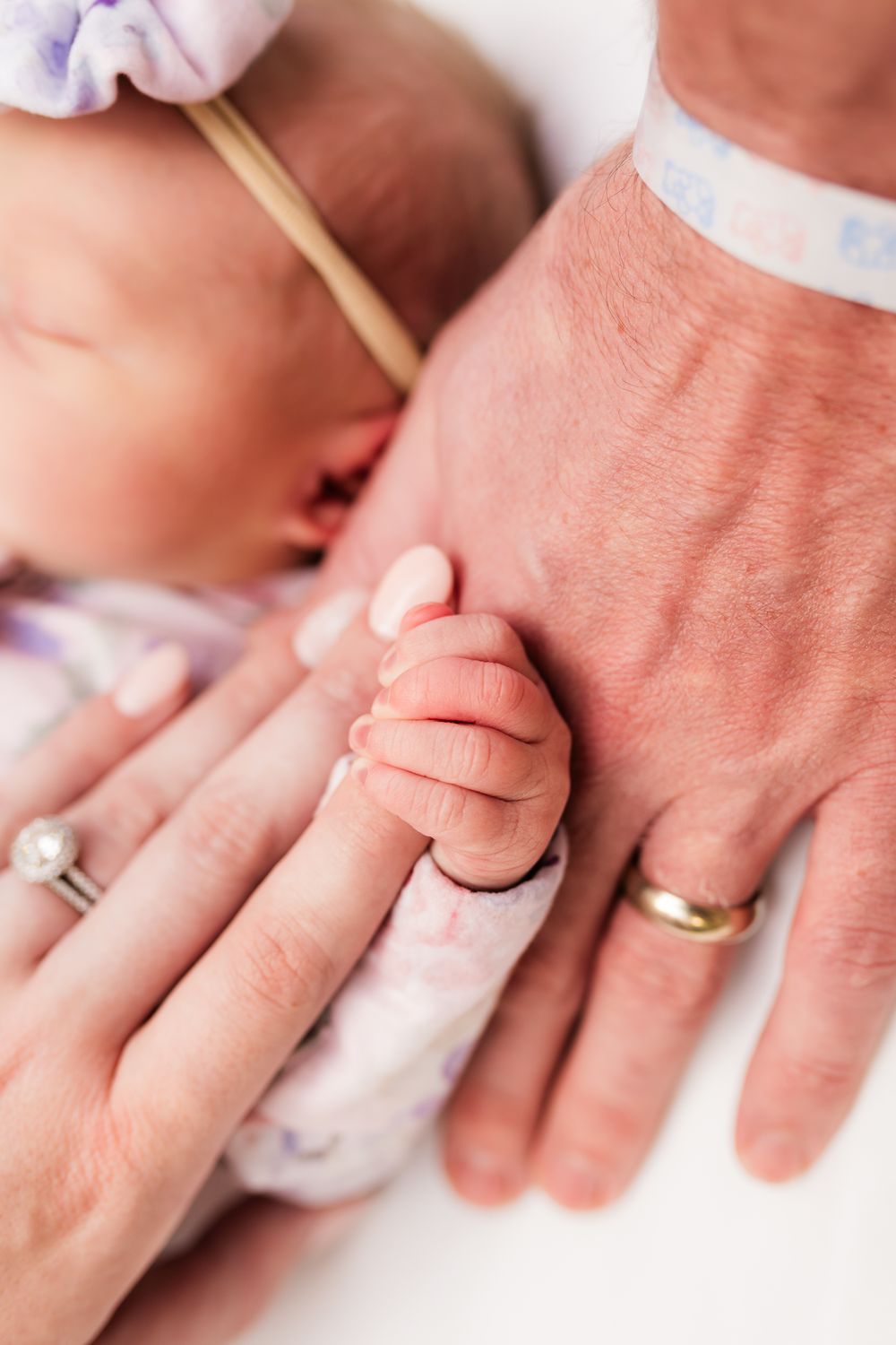 Close-up shots of tiny newborn fingers grasping adult hands wearing wedding rings.