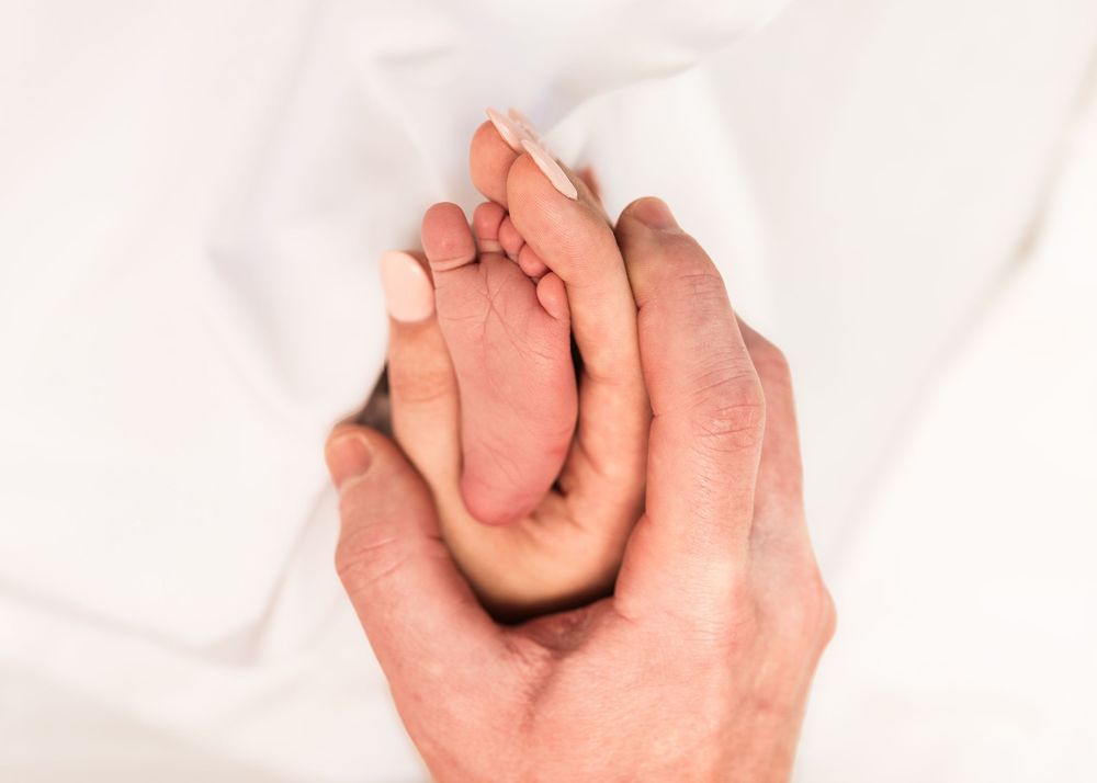 Gentle hand cradles sleeping newborn baby dressed in delicate floral clothing.