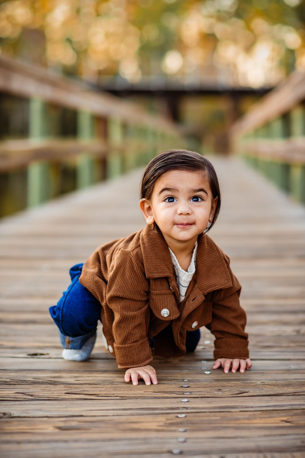 Small child in brown corduroy coat crawls playfully across wooden deck surface in sequence of action shots.