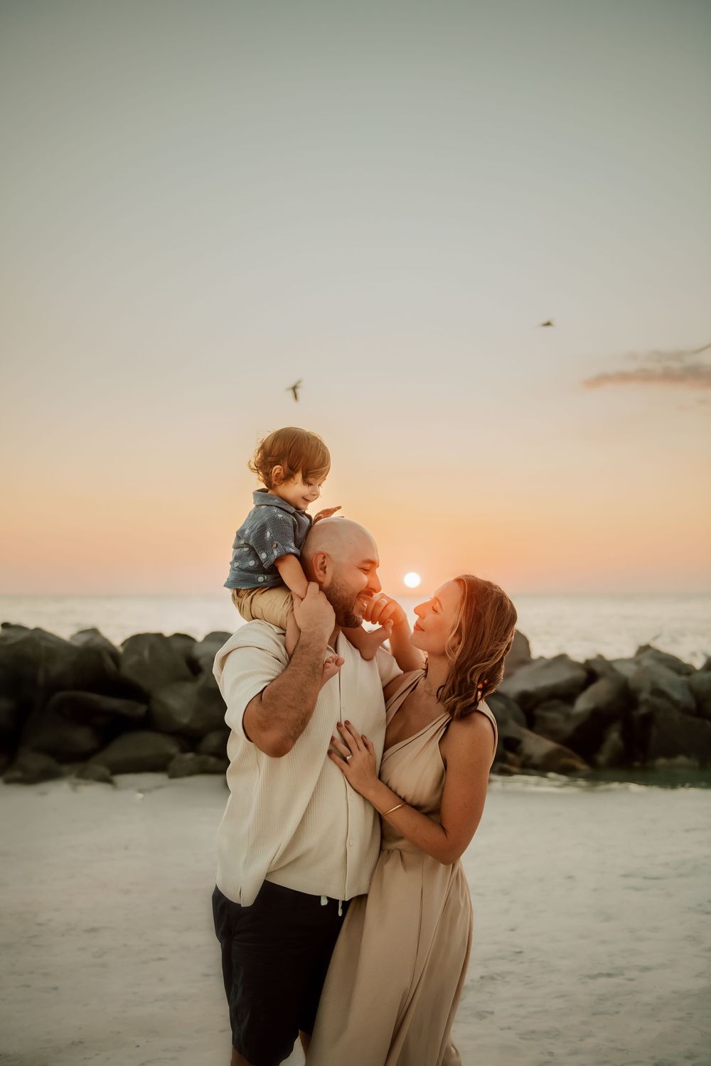 A loving family moment captured in a series of sunset beach photos with warm golden light and rocky shoreline.