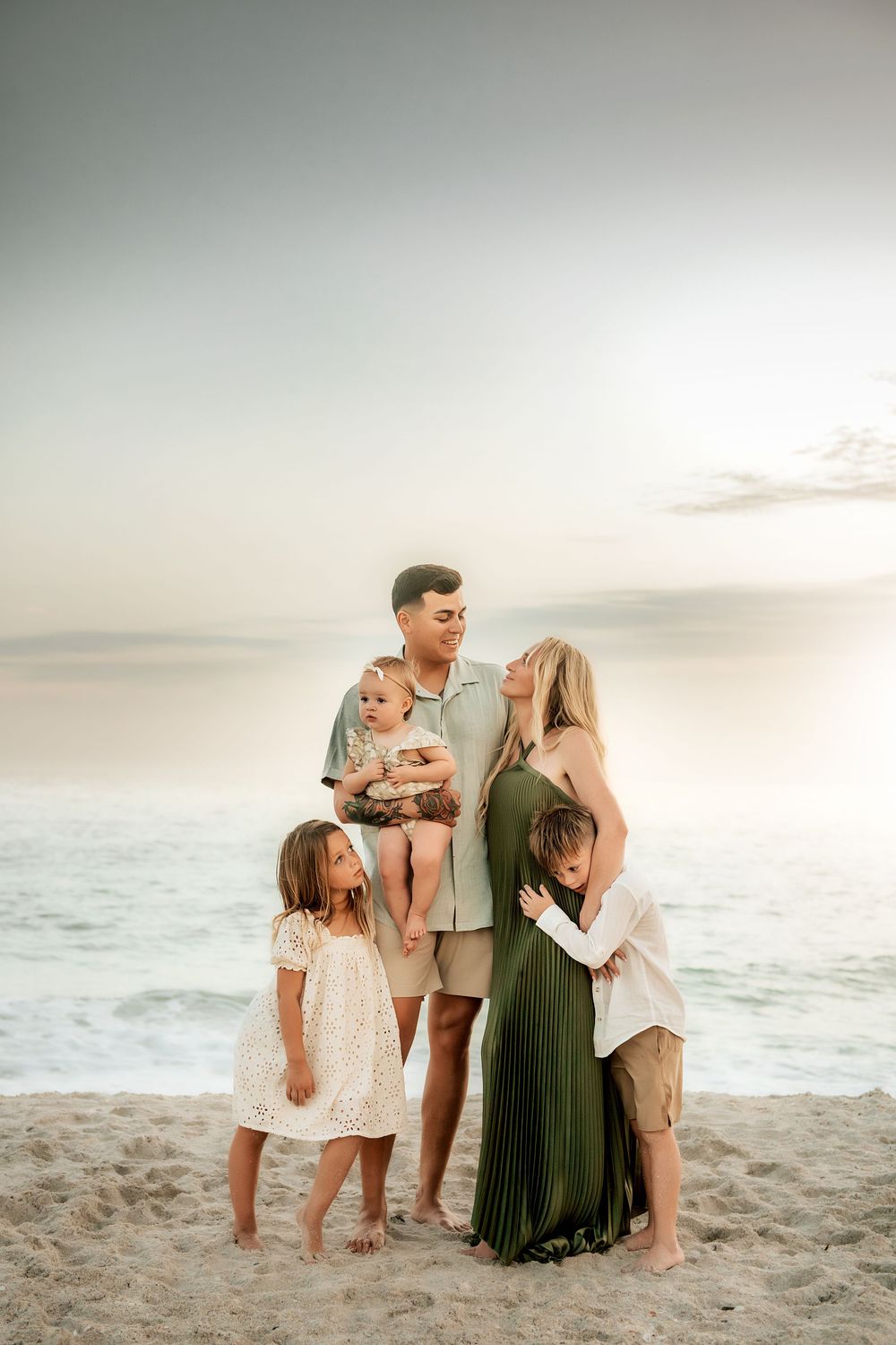 A family shares a tender moment together on the beach at sunset with waves crashing in the background.
