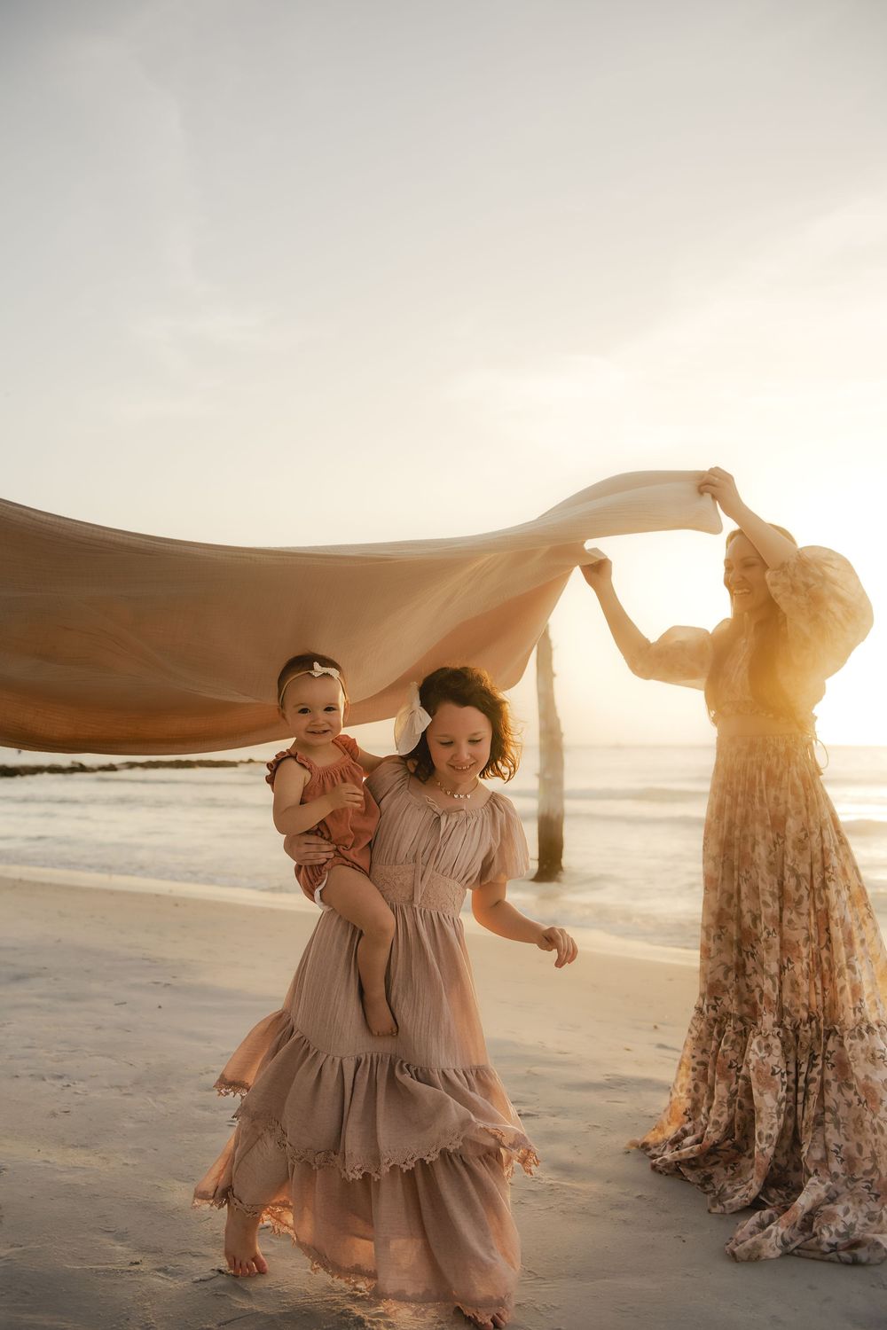 Ethereal beach scene with flowing fabric and dresses during golden hour as figures dance in gorgeous natural light.
