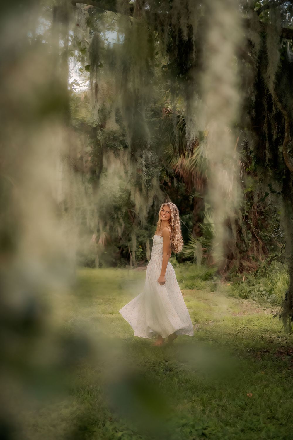 Ethereal white dress flows in a dreamy forest setting with Spanish moss and filtered sunlight creating a magical atmosphere.
