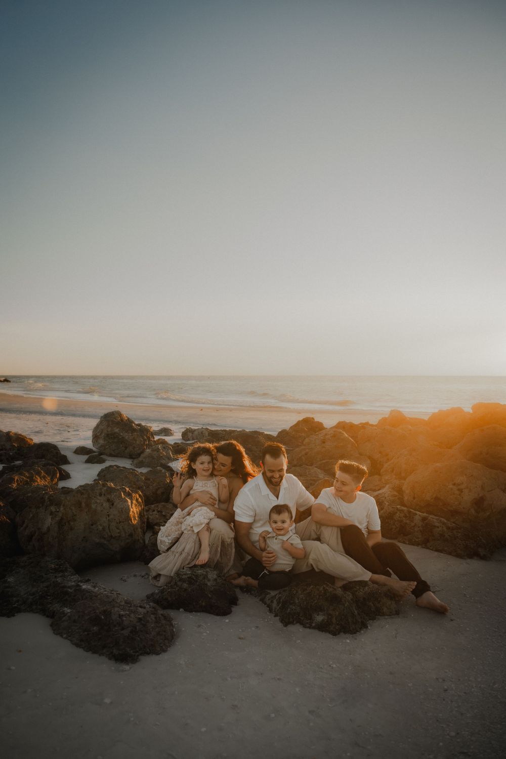 Family relaxes together on coastal rocks during sunset golden hour.