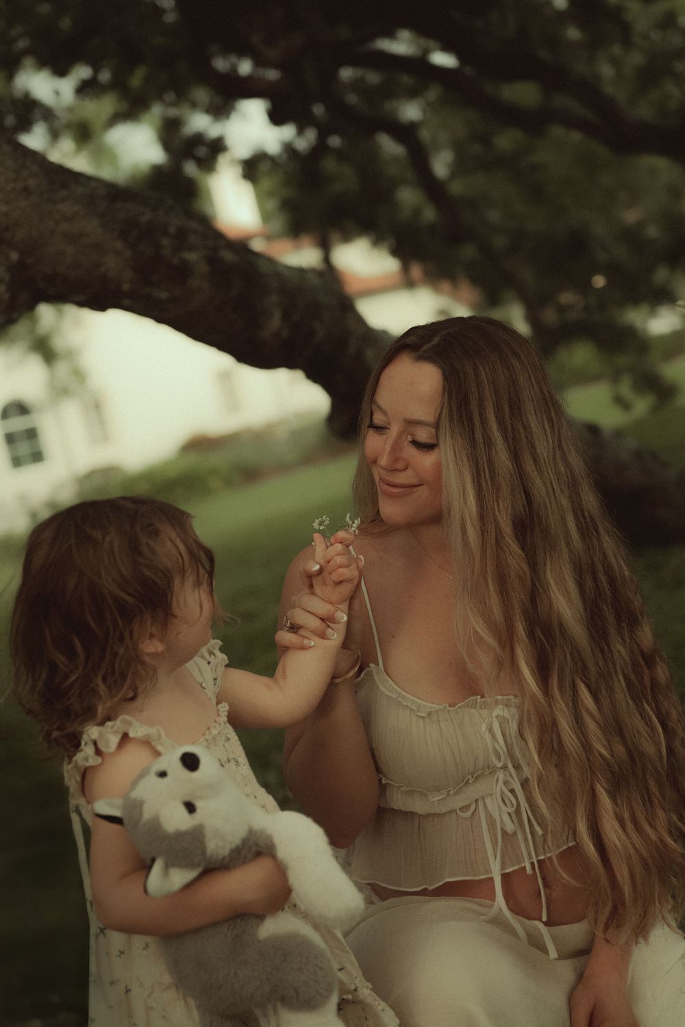 A tender outdoor moment between parent and child holding a stuffed animal on a summer afternoon beneath a tree.