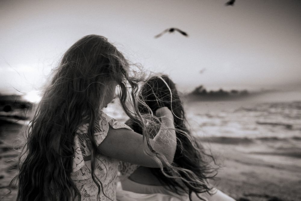Long-haired figure silhouetted against beach sunset with bird flying overhead.