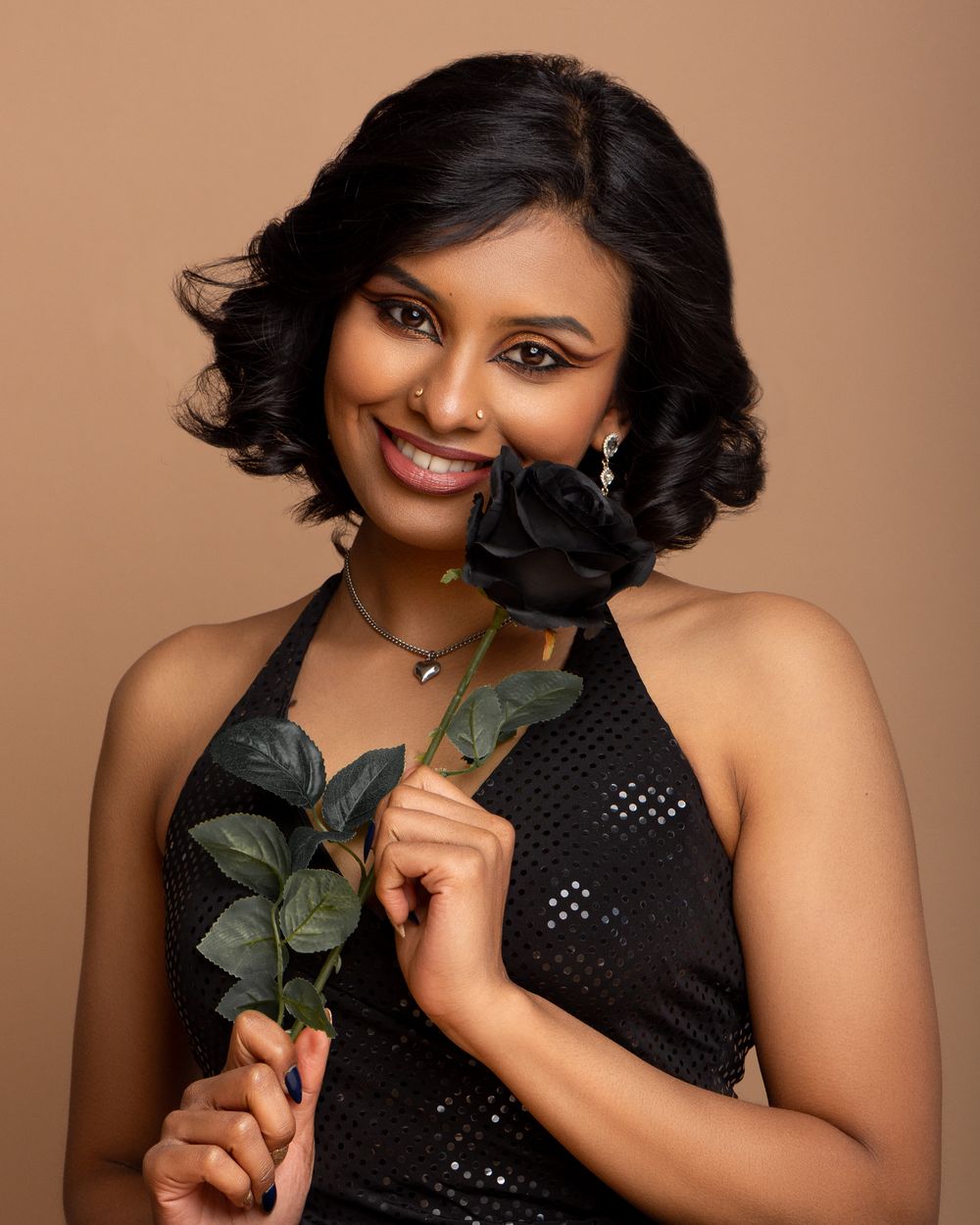 Woman in a black sequined dress poses against beige background while holding a dark rose for an elegant portrait series. Cambridge, UK