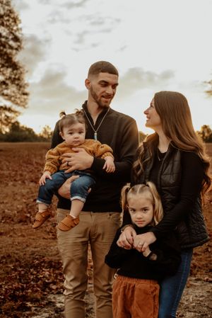 A young family poses together outdoors during golden hour on an autumn day.