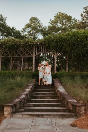 Family portrait on stone steps surrounded by lush garden landscaping at sunset.