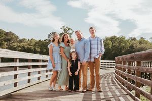 Family group photo on wooden bridge with matching blue and neutral outfits.