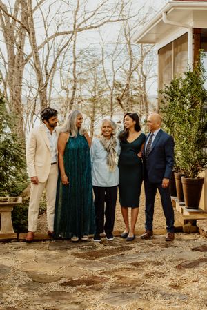 A happy group of five people in formal attire gather for a photo on an outdoor porch.