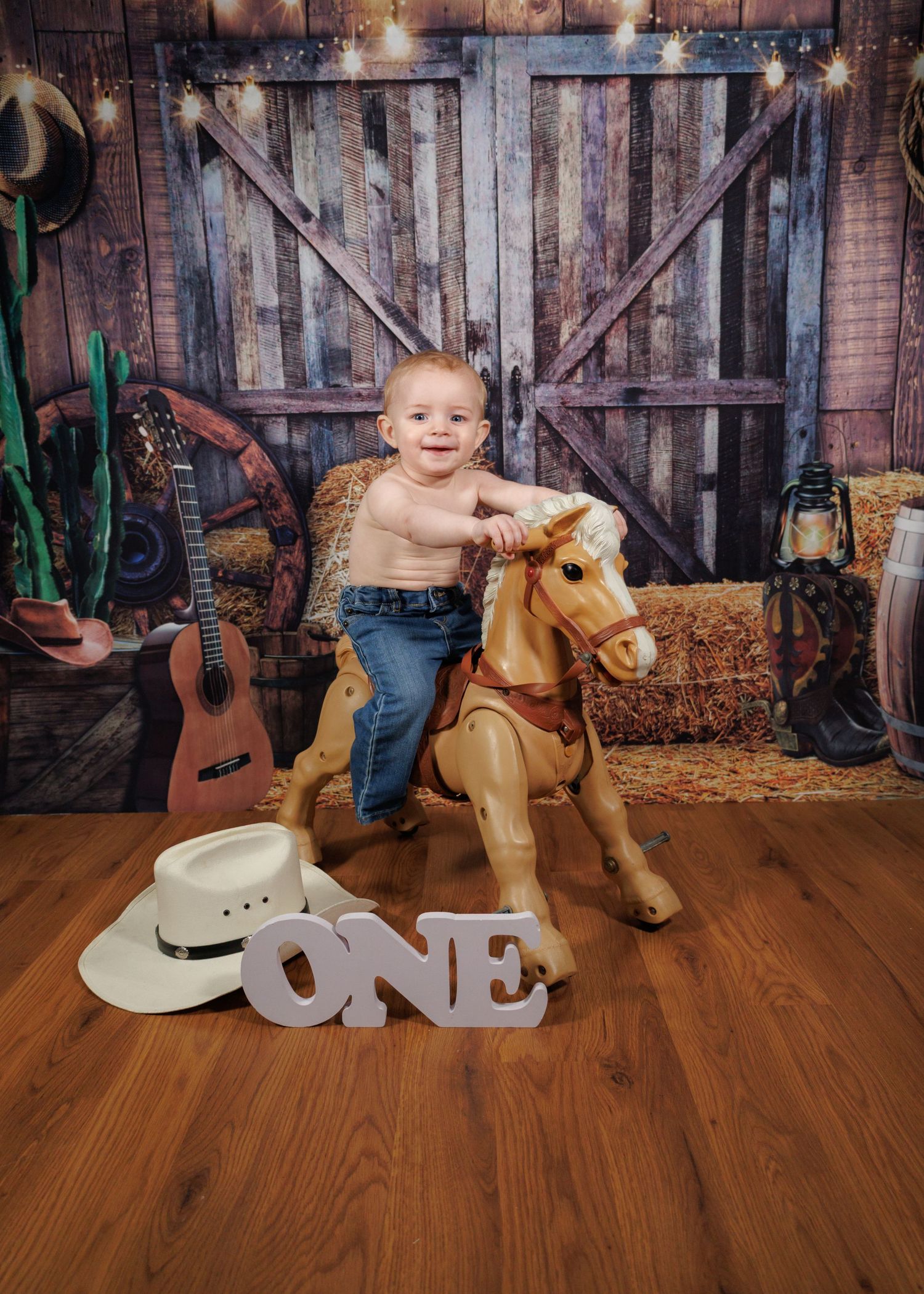 A western-themed first birthday photo with a rocking horse, guitar, and decorative wooden backdrop.