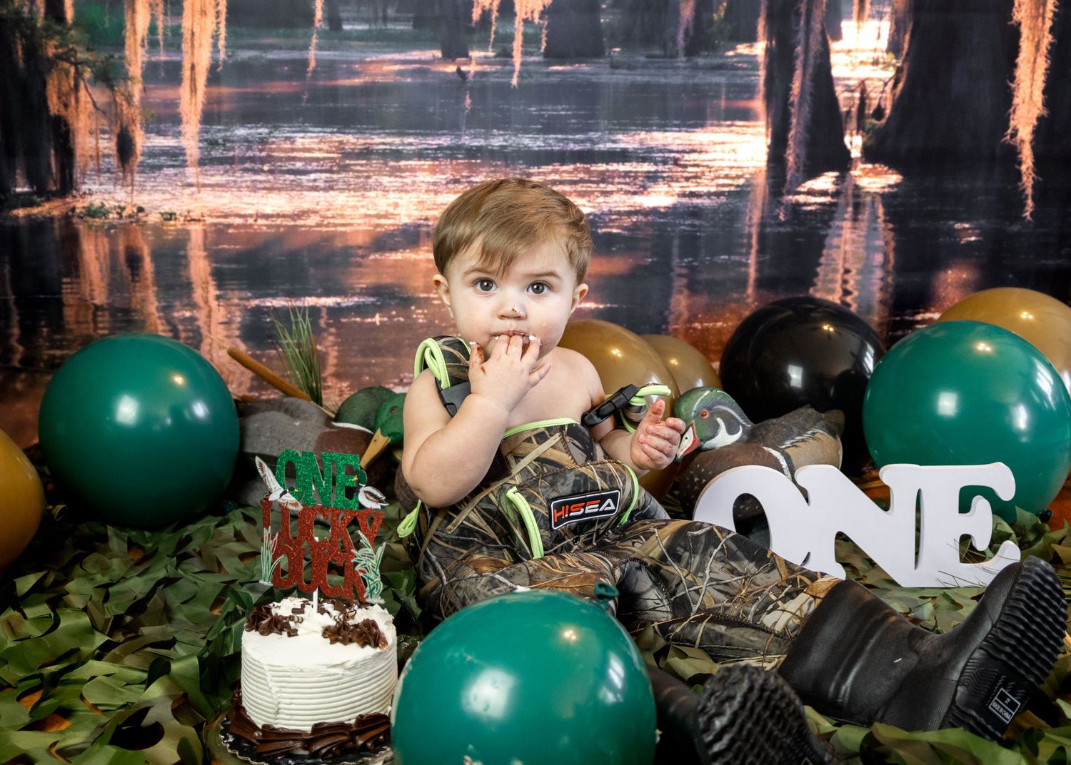 First birthday celebration setup with green balloons and woodland decorative elements.