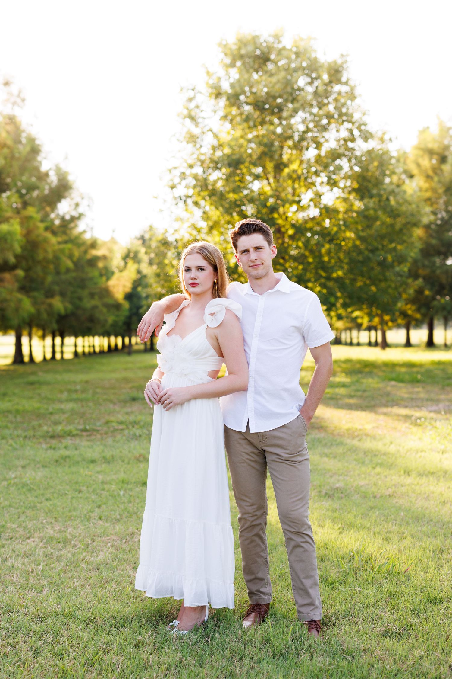 Family group in white and neutral clothing poses together in sunlit park setting.