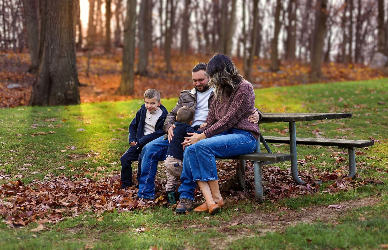 Family relaxing together on a wooden picnic bench in a park during fall season.