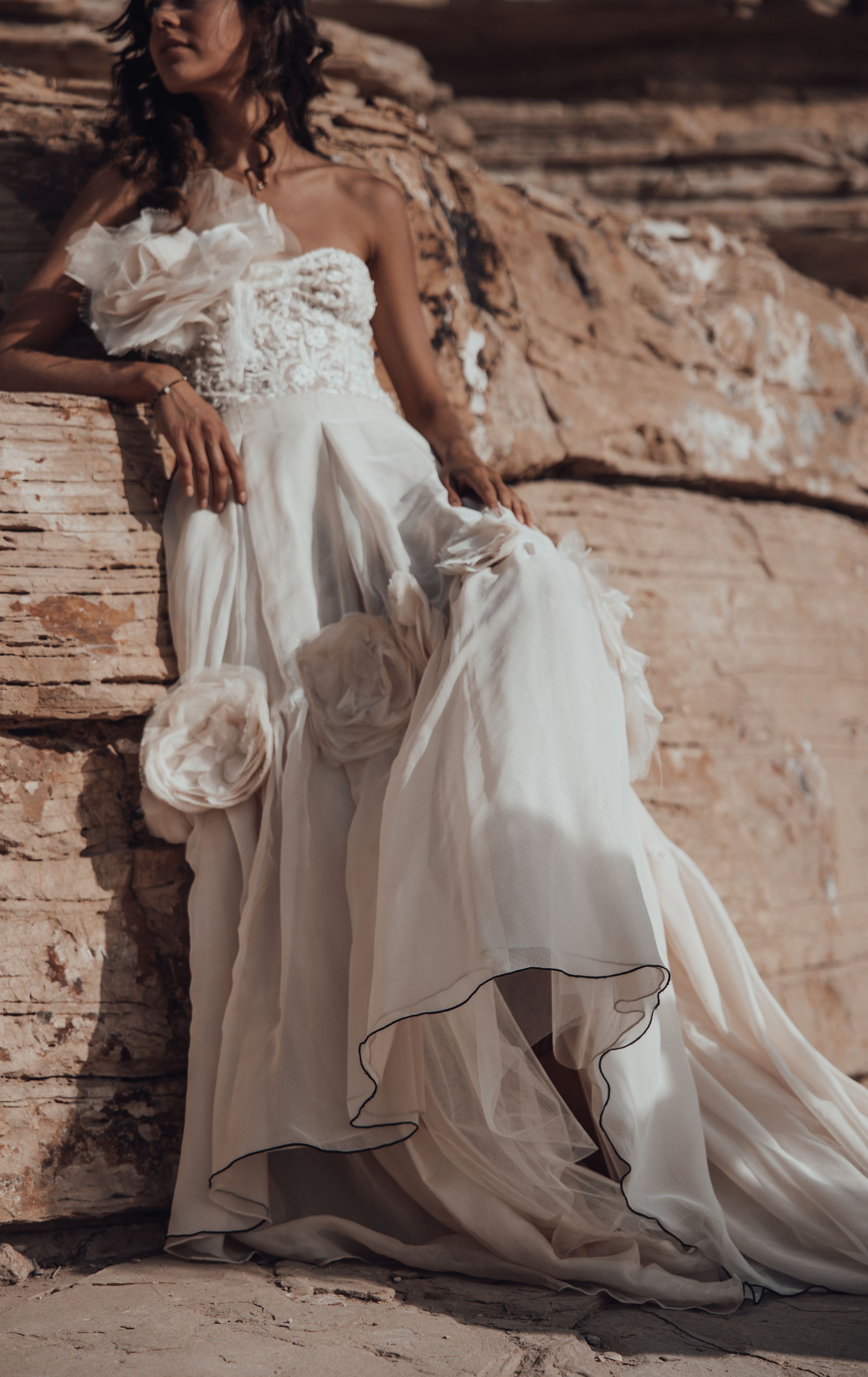 A flowing white wedding dress cascades over desert rocks in dramatic fashion.