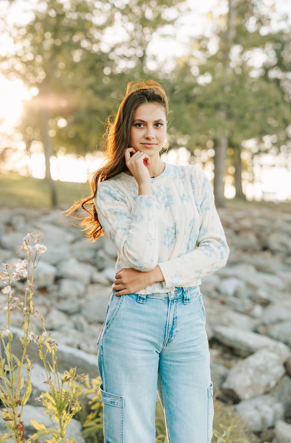 A casual outdoor portrait in tie-dye sweater and jeans against a golden sunset with rocks and trees in the background.