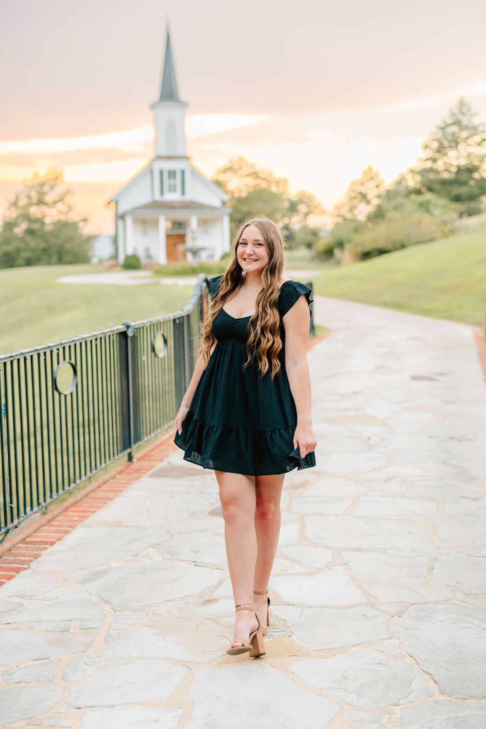 A black dress against the backdrop of a white chapel with steeple and golden sunset sky.