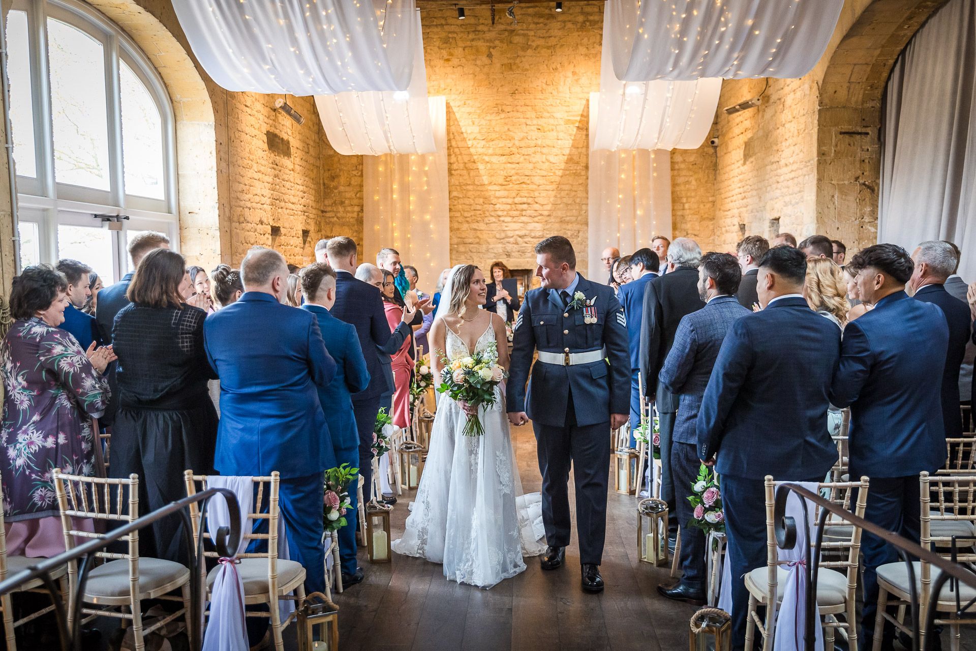 Indoor wedding ceremony at Lapstone Barn in the elegant stone-walled barn with white draping and natural light.