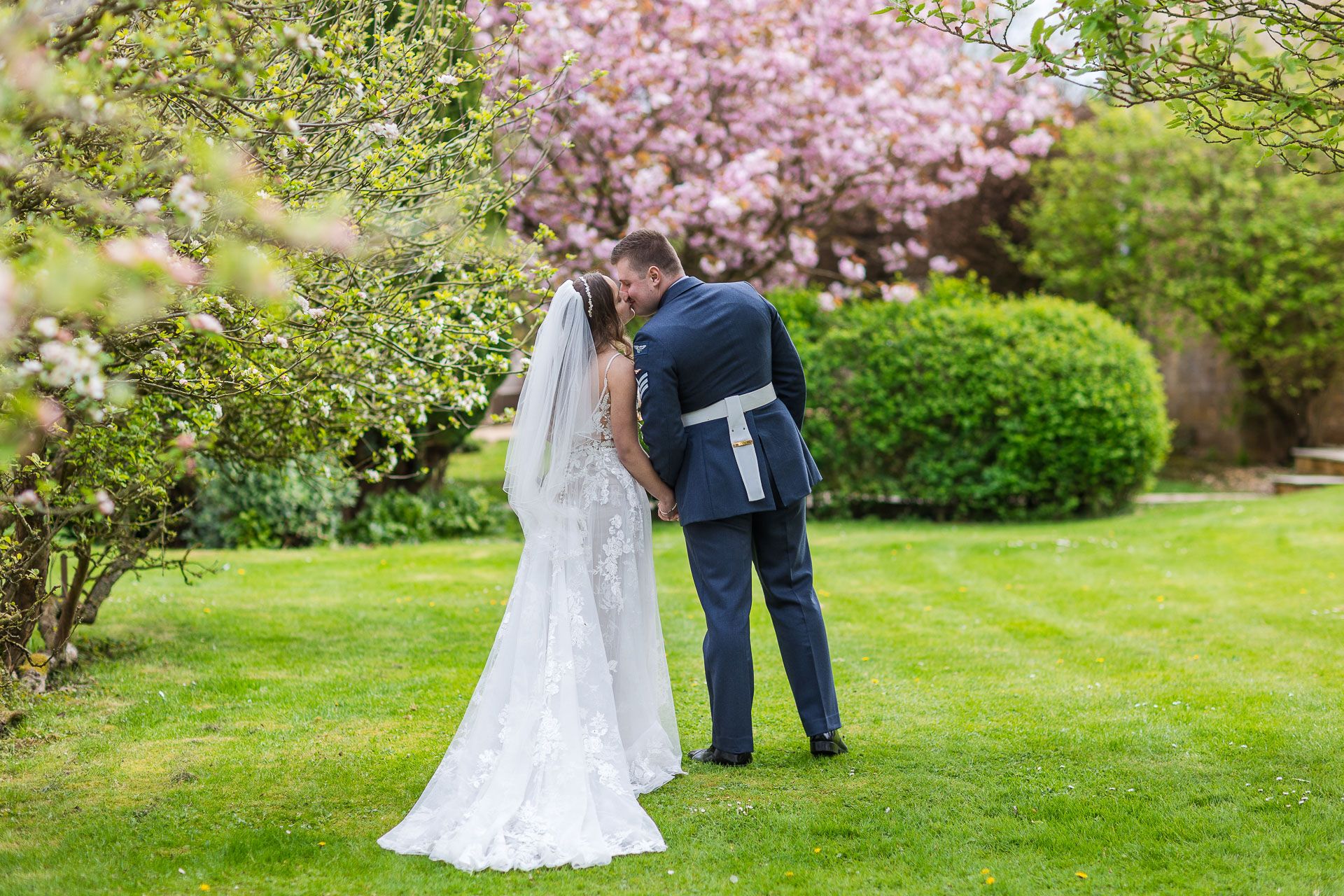 The bride and groom share a romantic moment under blooming cherry blossom trees in the lush garden at Lapstone Barn.