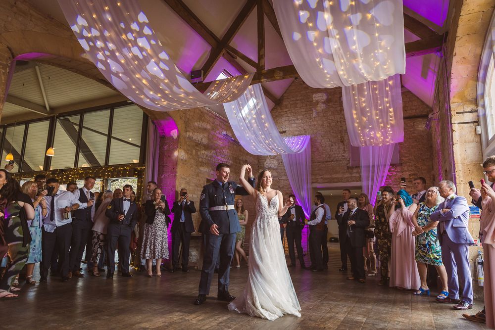 Wedding guests dance and celebrate on an illuminated dance floor under crystal chandeliers at Lapstone Barn in the Cotswolds.