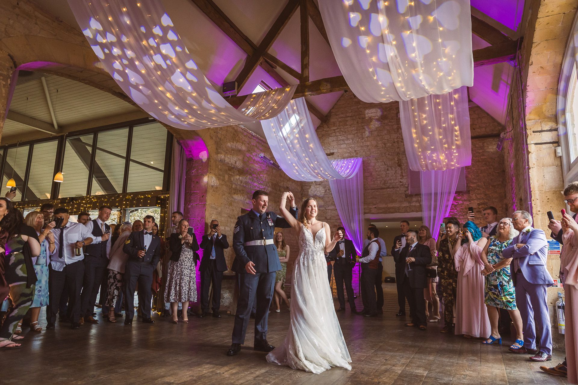Wedding guests dance and celebrate on an illuminated dance floor under crystal chandeliers at Lapstone Barn in the Cotswolds.