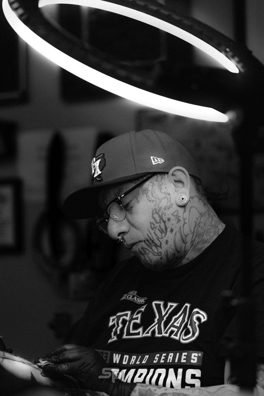 Black and white portrait under a circular LED light showing a person wearing a New Era cap and Texas World Series Champions shirt.