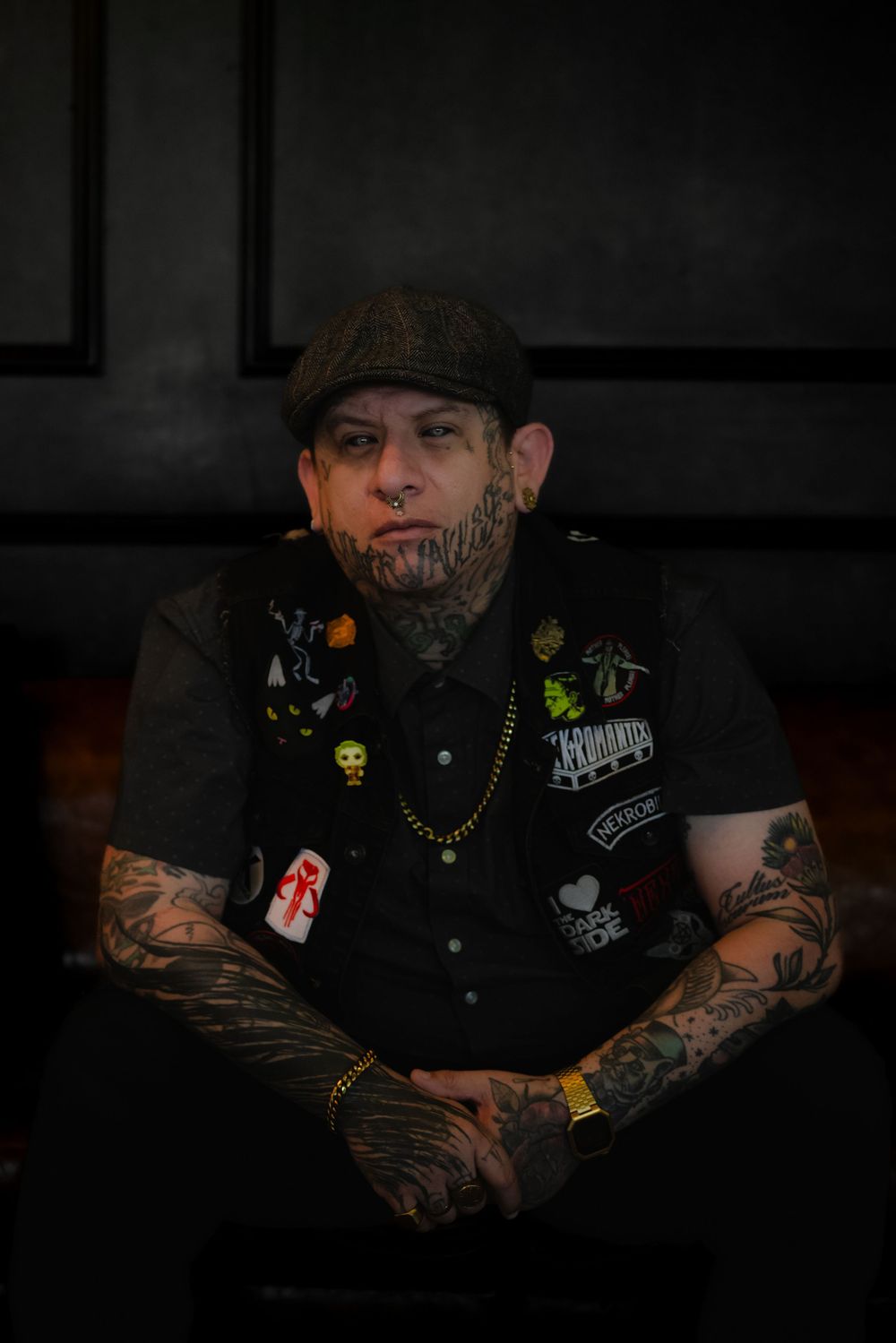Dark, moody portrait series showing figure in black clothing with tattoos and flat cap against shadowy background.