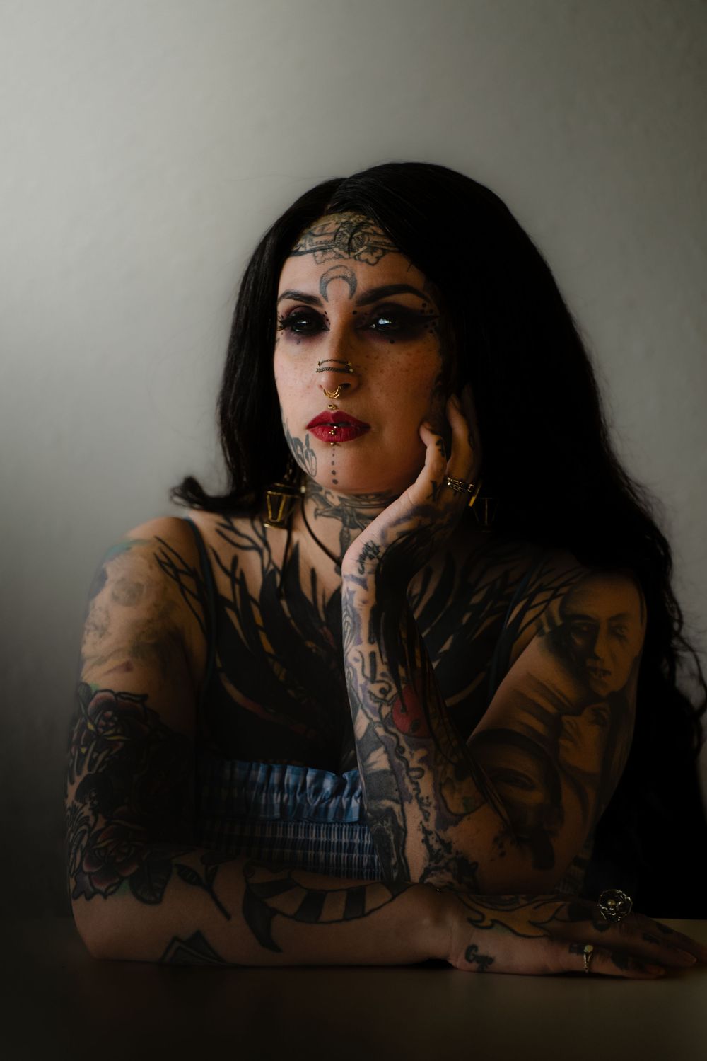 Moody portrait featuring dramatic makeup, intricate tattoos and gothic fashion in dark atmospheric lighting.