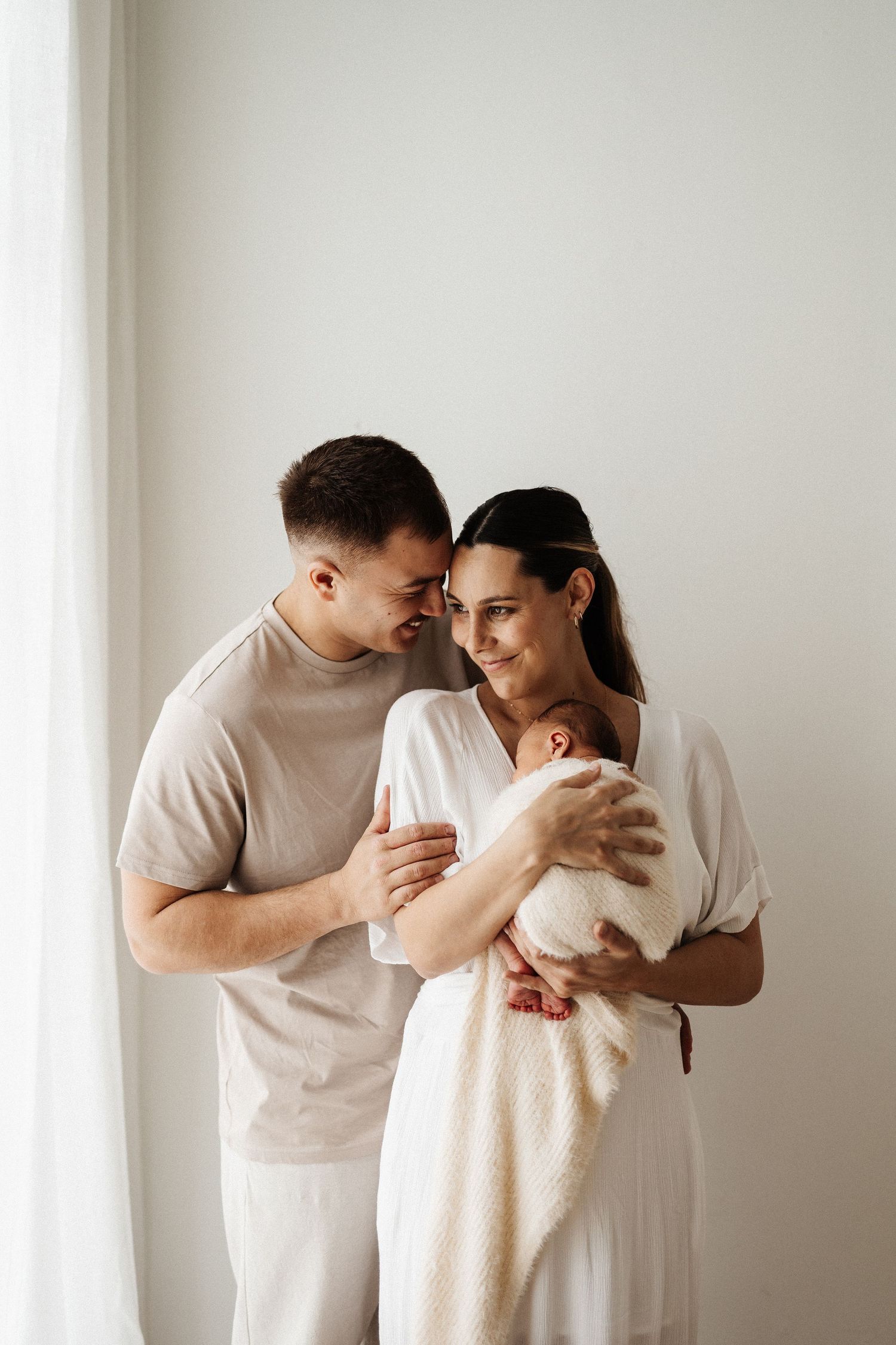 Mother in white dress sitting on floor with laughing baby in neutral studio setting.