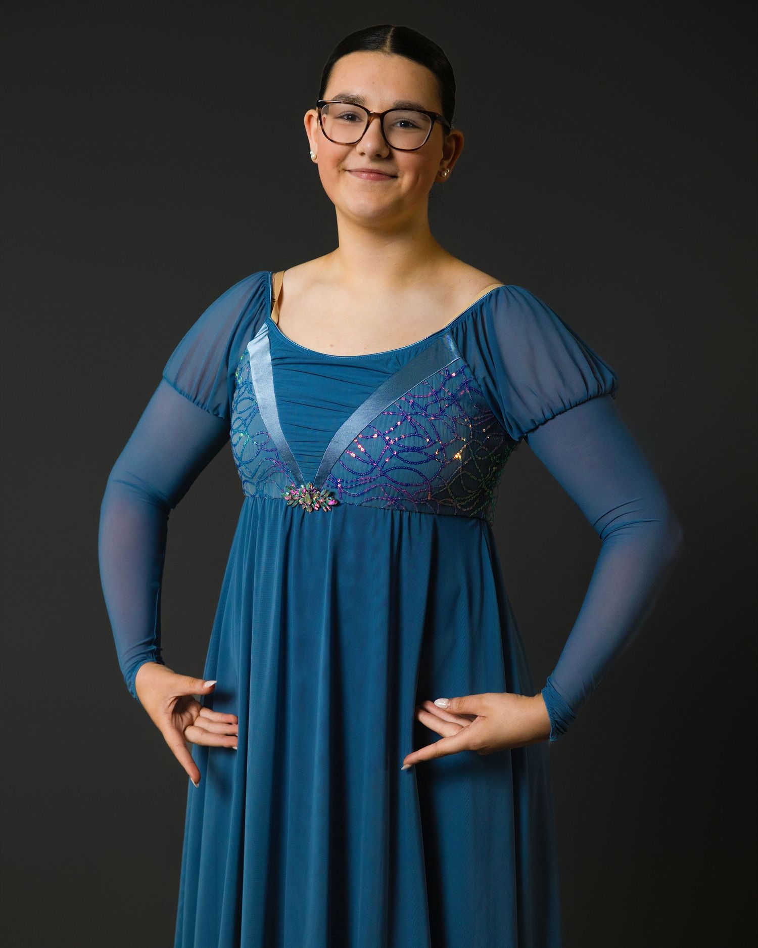 A dancer in a green velvet dress strikes an elegant pose with extended arms.