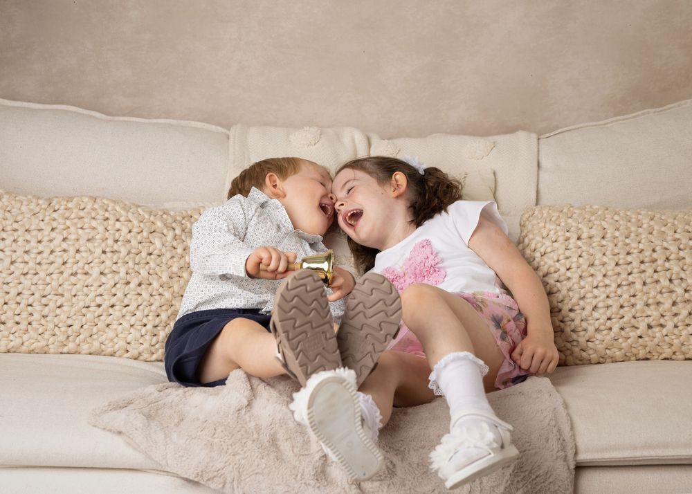 Two laughing children in socks laying on a couch with a beige knitted blanket.