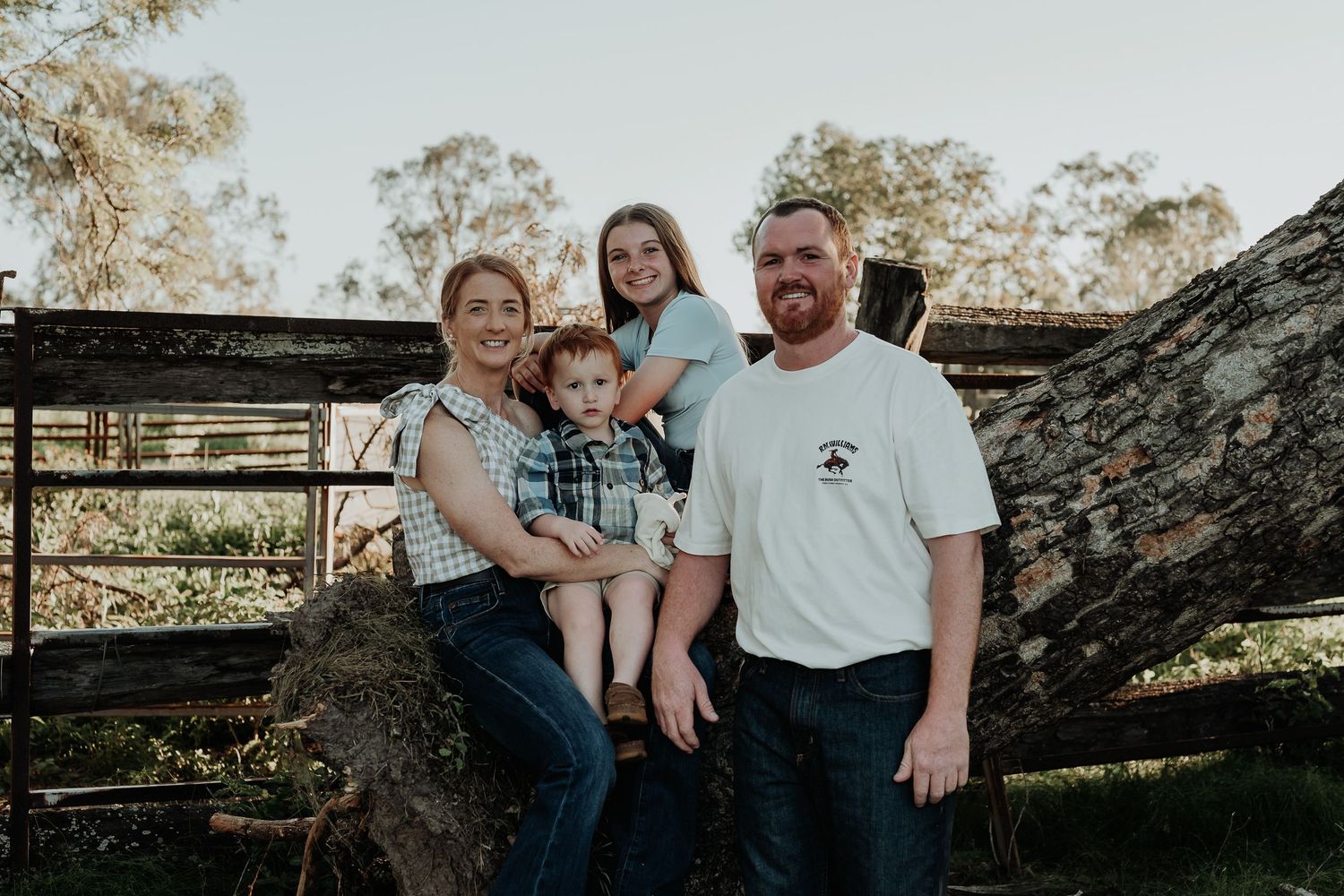 Family portrait session outdoors with rustic wooden fence and natural scenery.