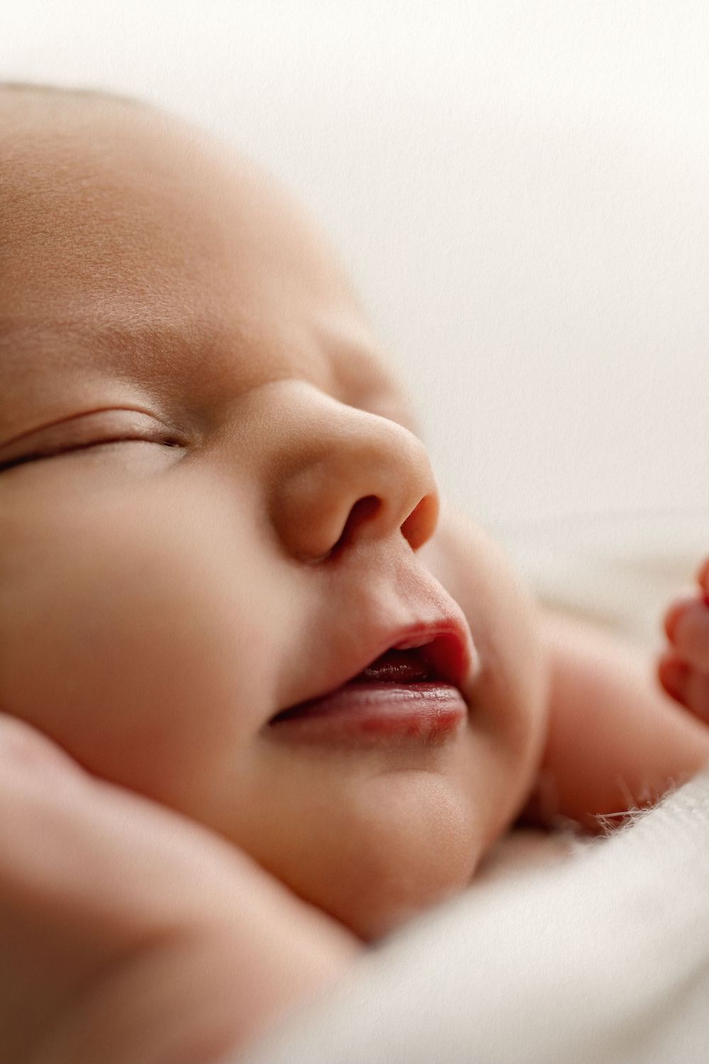 Close-up of a peaceful sleeping newborn baby with soft skin resting on a white blanket.