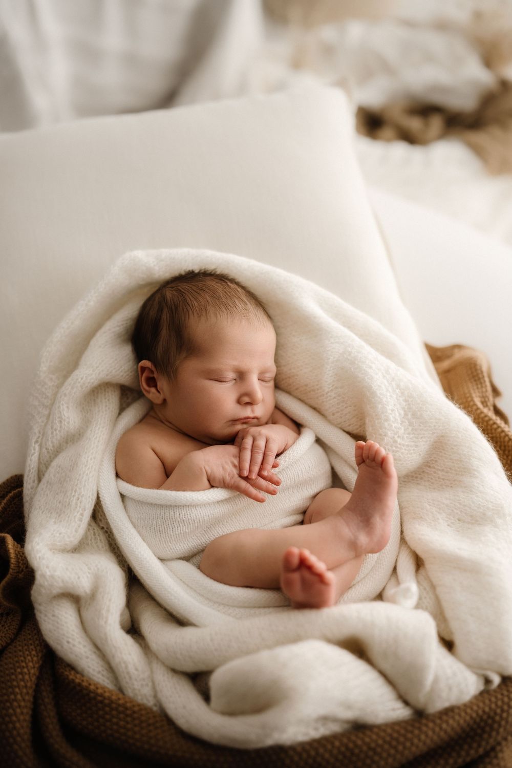 Peaceful newborn baby sleeping wrapped in a soft white knit blanket on a cozy bed.