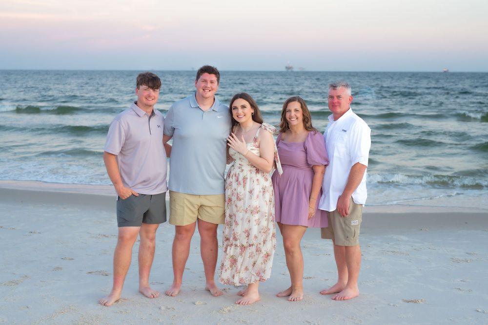 A group of people pose together on a beach at sunset with the ocean waves in the background.