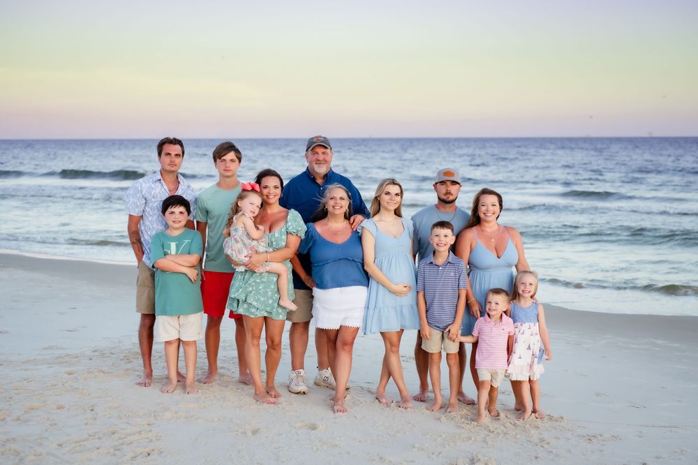 A group of happy people standing together on a sandy beach at sunset with ocean waves in the background.
