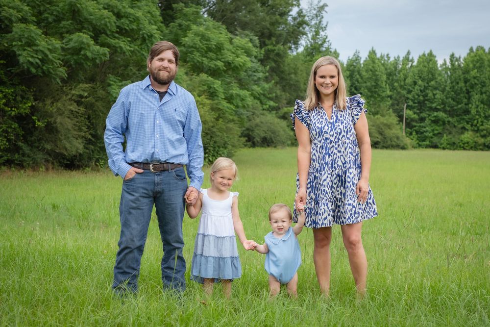 Family enjoying a sunny day together in a lush green meadow, walking hand in hand through the grass.