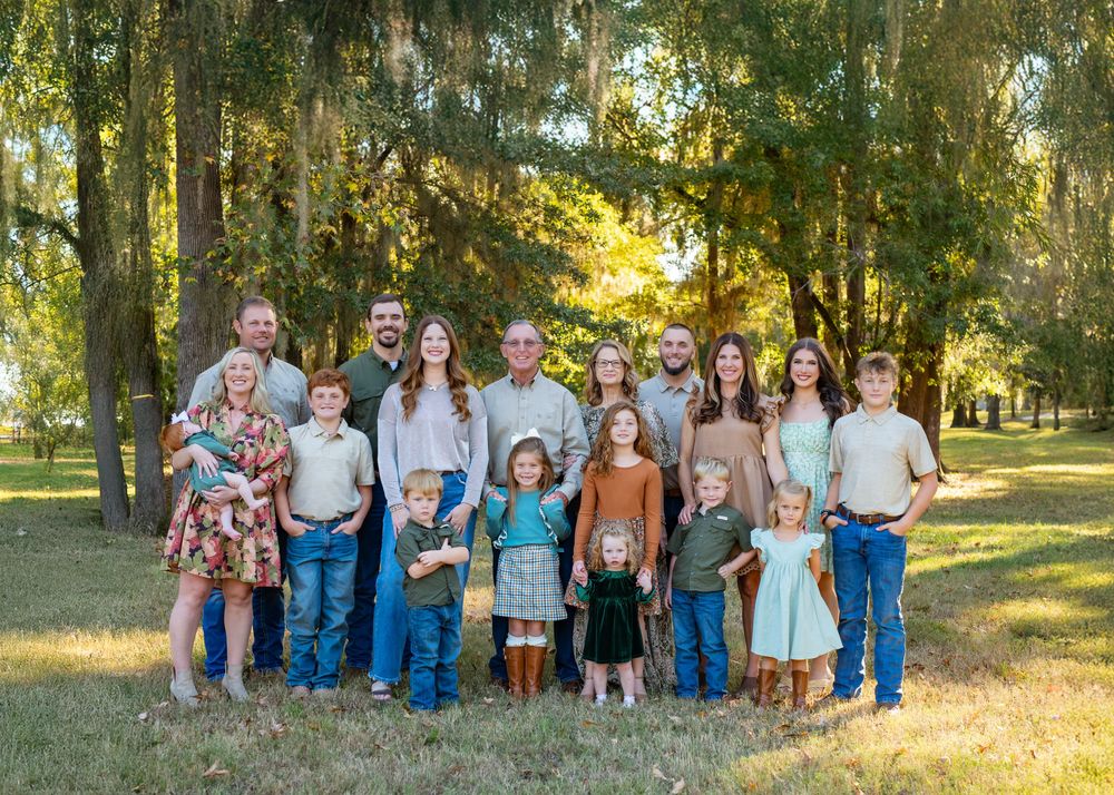 A panoramic collage of people posing together outdoors in a grassy field with sunlit trees in the background.