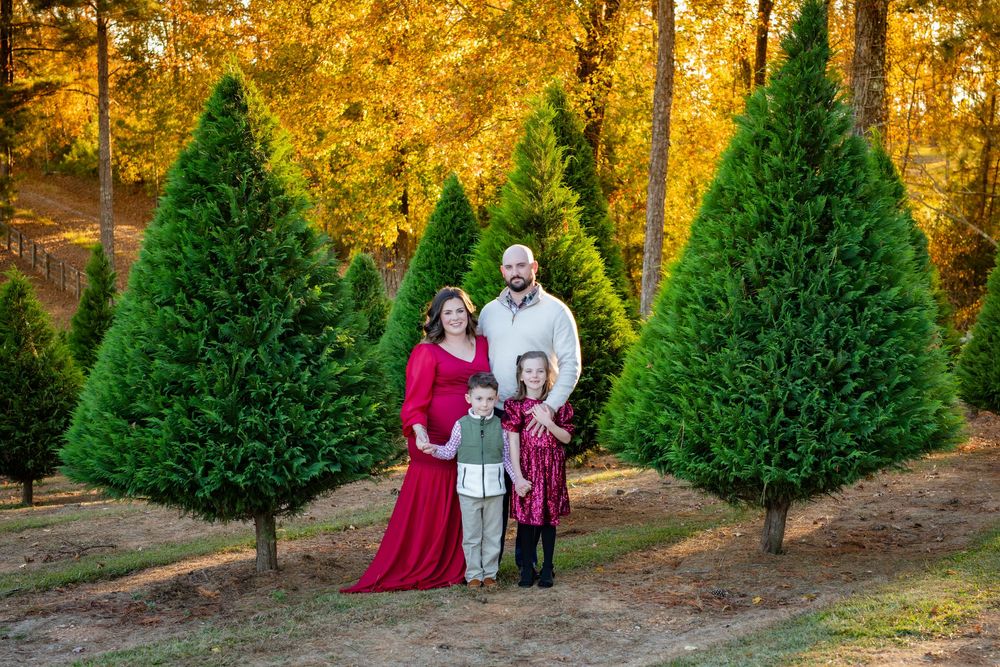 A group stands among evergreen trees with golden autumn foliage in the background during a fall photoshoot.