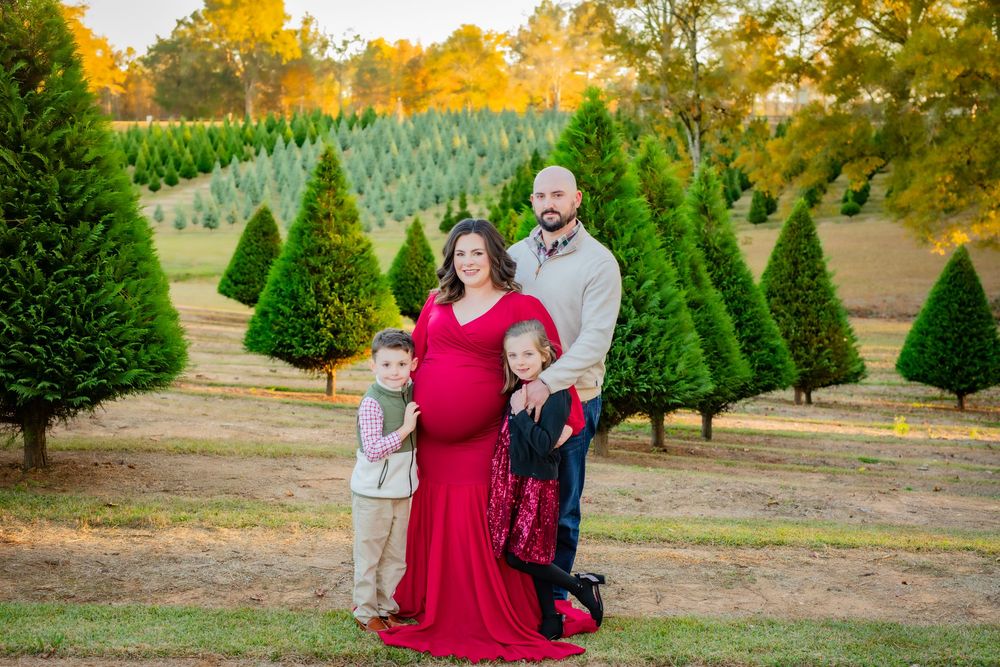 Family poses together among evergreen trees at Christmas tree farm during golden autumn sunset.