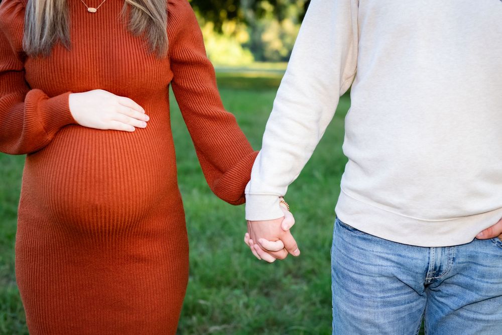 Couple in casual fall attire holding hands while walking in a park setting with green grass.