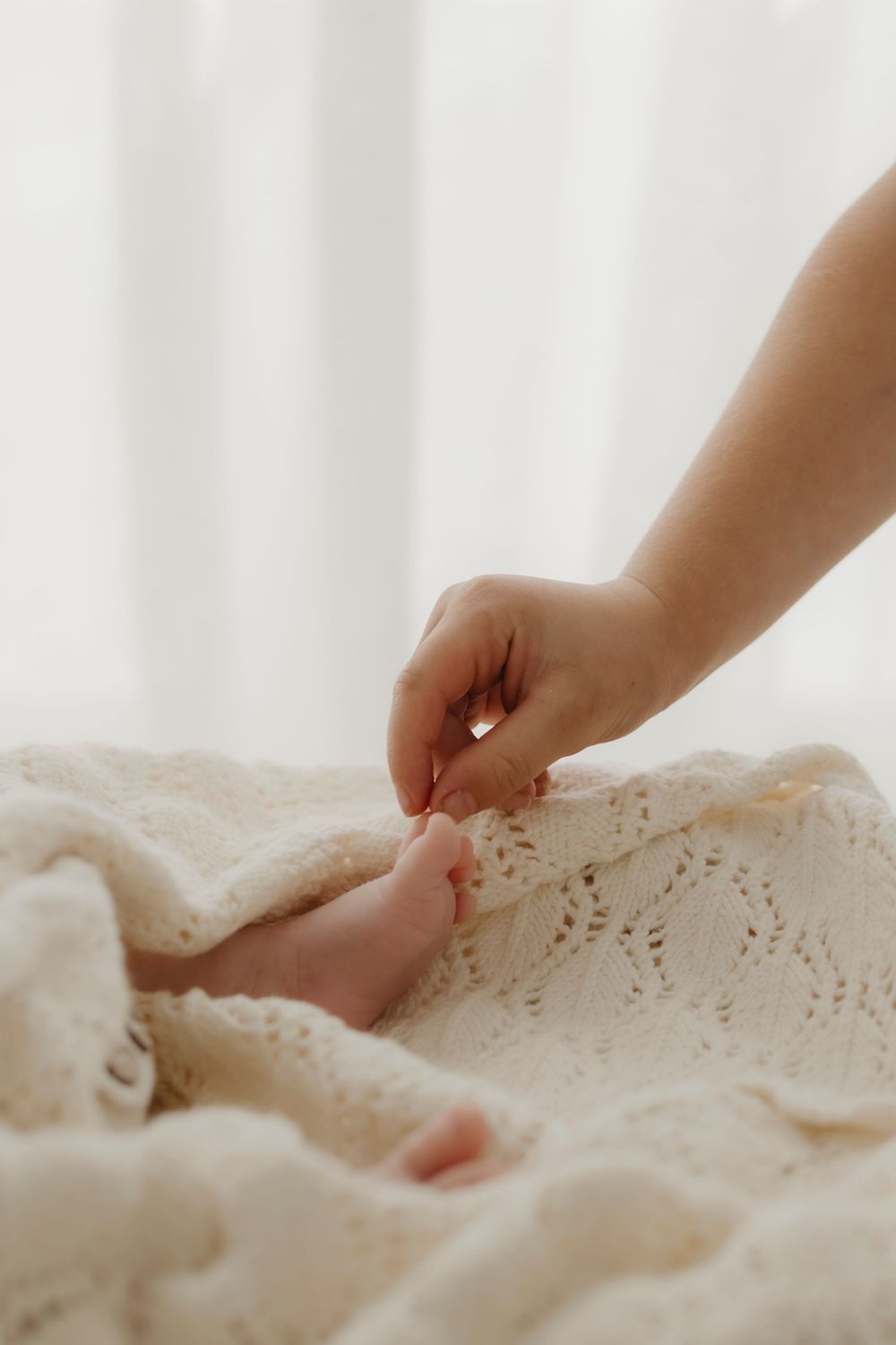 A child's hand gently touches a newborn baby's tiny feet resting on a cream lace blanket.