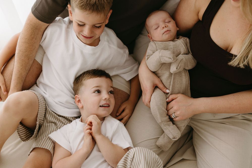 Two young brothers lying beside sleeping newborn sibling held by parents.